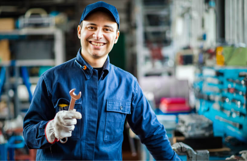 A maintenance worker in a machine shop smiling and holding a wrench.
