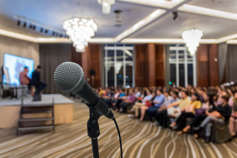 A closeup of a speaker's microphone in front of a crowd at a conference.